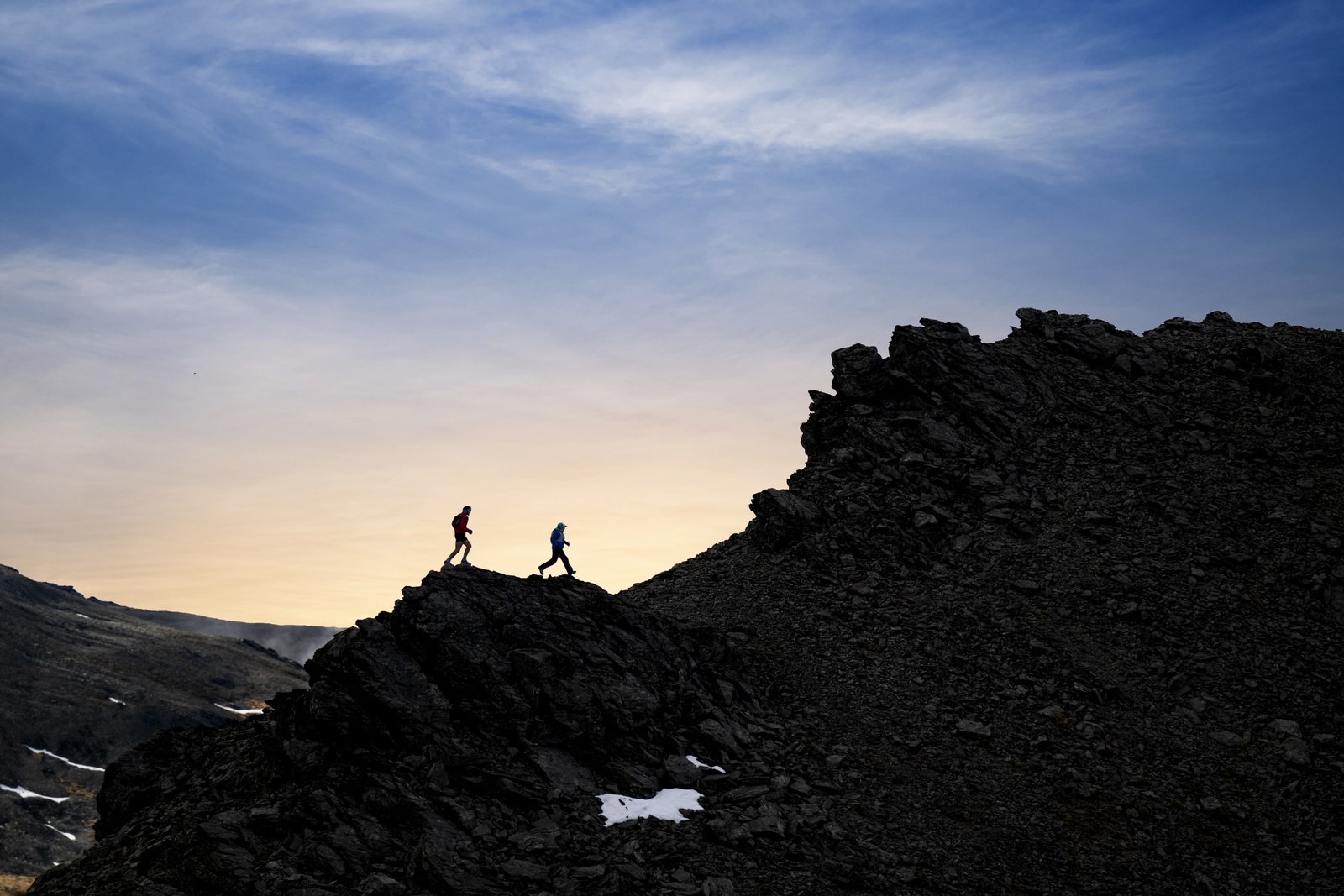 Två löpare längs en bergsrygg i kvällsljus